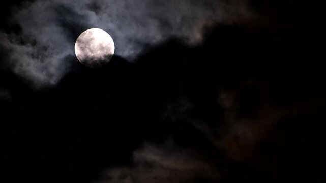 Full moon in dark night sky with ominous foreboding clouds passing by, telephoto