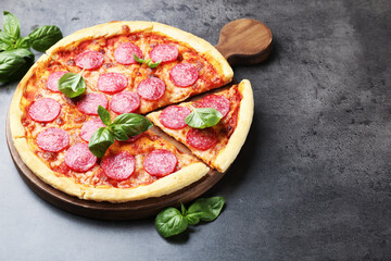 Delicious cut pepperoni pizza with fresh basil on grey table. Space for text
