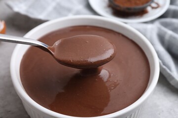 Taking liquid chocolate dough from bowl with spoon on grey table, closeup