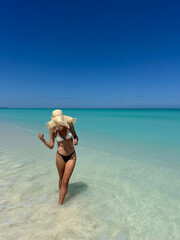 A woman standing on a beautiful tropical beach in Madagascar with clear turquoise water and white sand. The bright sunlight, blue sky, and crystal-clear ocean create a peaceful and exotic summer 