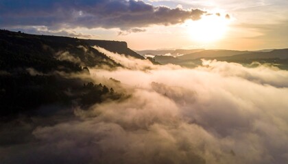 Fototapeta premium Breathtaking sunrise over mountain cliffs covered in mist and clouds, capturing the beauty of nature’s serenity and the calm morning atmosphere