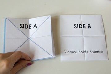 Two white paper sheets with folds and labels laid out for a craft or geometry lesson