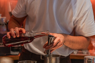 Bartender pouring red liquid into jigger for cocktail preparation