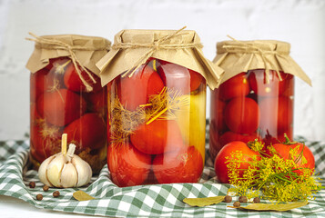 Homemade pickled tomatoes with garlic, dill, and spices in jars on the kitchen table. Traditional autumn food storage. Close-up.
