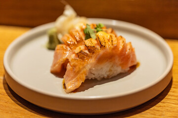 Grilled salmon sushi on a white plate with wasabi and ginger garnish