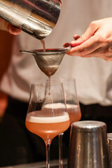 Bartender pouring cocktail through strainer into glass with foam