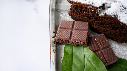Macro view of chocolate bars with chocolate cake on ceramic plate on white marble surface, sweet dessert and cocoa pastry flat lay, selective focus
