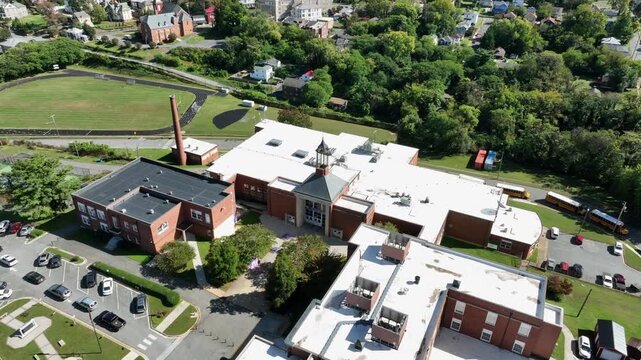 Aerial orbit shot of american high school of Lynchburg near city neighborhood and grass in park. Sunny day in autumn season. Wide shot. Virginia, USA. Parking cars on area.