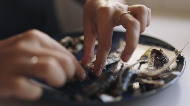 Person's hands cleaning small fish on a plate