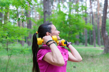 A happy mature woman lifting dumbbells in a green park, enjoying her workout and staying active.