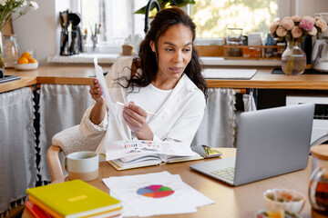 Professional businesswoman using laptop, working at home in kitchen showing graphs having video call