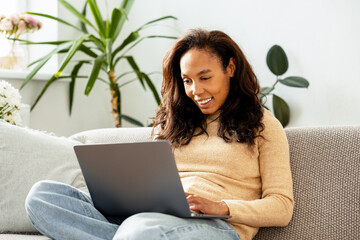 Successful smiling African American woman using laptop checking mail, copywriter typing on keyboard