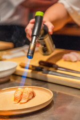 Sushi chef using torch to sear salmon sushi on a plate in kitchen