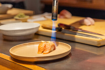 Culinary artist using torch to sear salmon sushi on wooden countertop