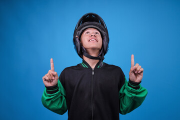 Portrait of Cheerful Asian Man Wearing Helmet, Looking up and Pointing Both Index Fingers Skyward