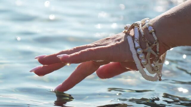 Hand water summer. Female hand wearing beach bracelets gently touching clear sparkling ocean surface