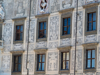 Fototapeta premium Palazzo della Carovana facade displaying intricate sgraffito decoration, presenting winged female figures, garlands, and vases on a textured wall, framing two tall windows