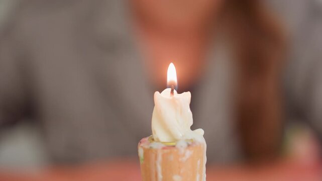 close up candle flame burns on wax stub with soft bokeh person in background, warm glow and melting drips on wooden holder during calm classroom moment, gentle focus and safety lesson