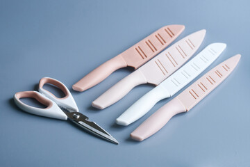 Set of modern pastel kitchen knives with silicone handles and blade covers placed beside kitchen scissors on neutral background, minimalist cooking tools concept. Photo
