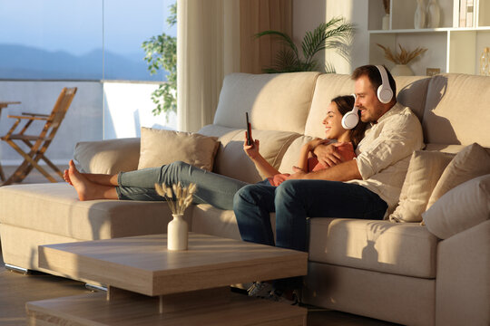 Happy couple sharing music checking phone on a couch