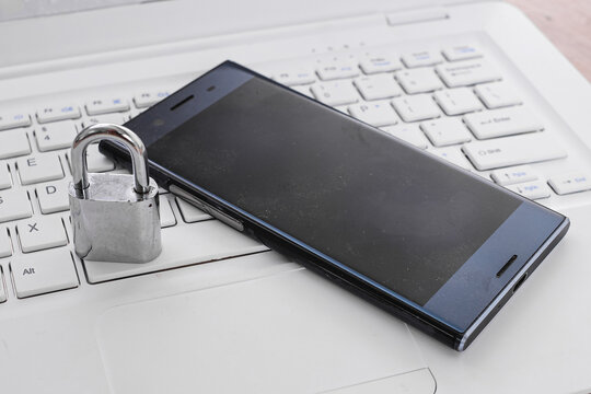 Close Up Of Locked Padlock, Smartphone, And Laptop Representing Cyber Security And Data Protection