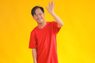 Cheerful Young Asian Man With Joyfully Waving Hello in Front of a Yellow Backdrop © Gatot