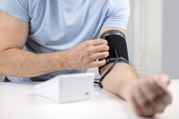 Hands with a tonometer on the table. Man in a shirt measures blood pressure with an electronic tonometer
