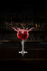 Red cocktail splash explosion in elegant bar interior with vivid droplets. Concept of nightlife energy, emotion, and celebration for HoReCa branding and advertising visuals.