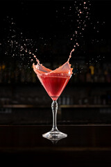 Red martini splash on bar counter with glowing droplets and reflection. Concept of vivid movement, excitement, and joy for beverage branding and design visuals.