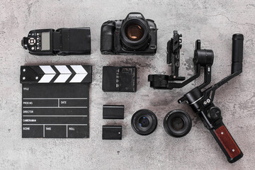 Flat Lay Of Filmmaker Gear With Camera, Gimbal, Clapperboard, Lenses, Flash Over Cement Background