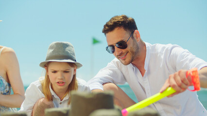 Father and son enjoying a summer beach vacation, bonding while building a sandcastle in the sand,...
