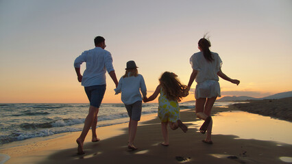 Family enjoying vacation running barefoot on a sandy beach, holding hands as the sun sets over the ocean, symbolizing freedom, togetherness, and happiness
