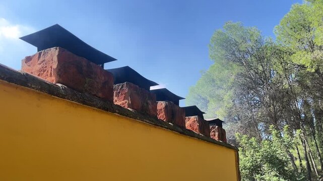 A row of chimneys are on a yellow wall