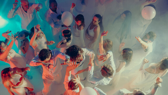 People dancing freely surrounded by lights and smoke at party. Concept of energetic youth culture, lifestyle expression, promotional visual for music and entertainment industries.