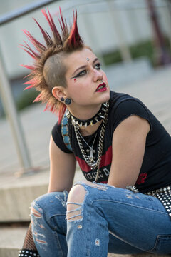 A young woman with a vibrant red and black mohawk sits thoughtfully, representing punk rock culture with her unique style and fashion