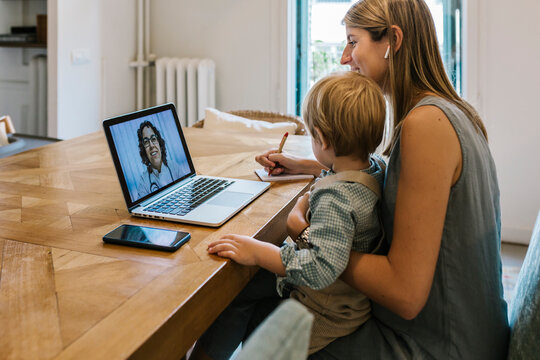 Female pediatrician assisting woman with son sitting at home