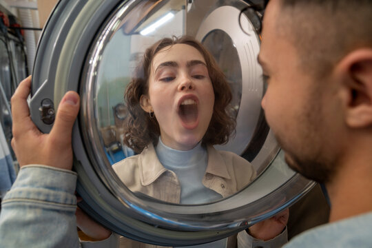 Young man looking at girlfriend breathing on washing machine glass in laundromat