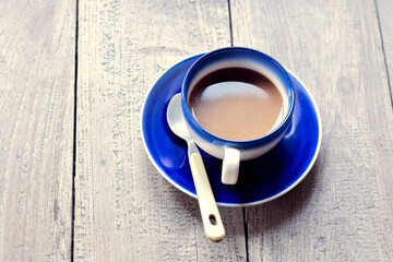 he drink is served in an elegant ceramic cup, which has a contrasting white base and a striking royal blue rim and interior. The cup sits atop a matching, glossy blue saucer.