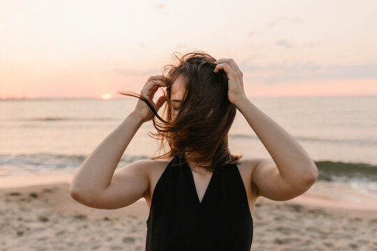 Woman standing on the beach at sunset with windblown hair