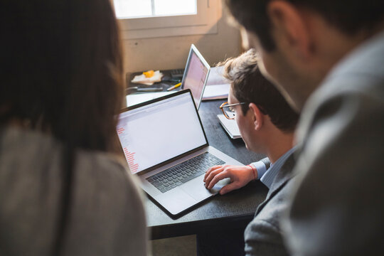 Three business people sharing laptop at desk in office