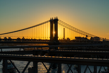 Obraz premium Golden Sunrise Light Bursts Through Manhattan Bridge Towers, Silhouetting the Iconic Structure Over New York City's East River