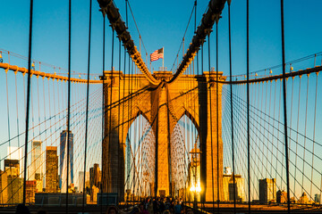 Iconic Brooklyn Bridge Towers Bathed in Golden Sunrise Light, Featuring American Flag and New York City Skyline