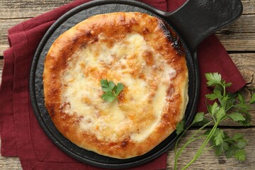 Delicious Megrelian khachapuri with parsley on wooden table, flat lay