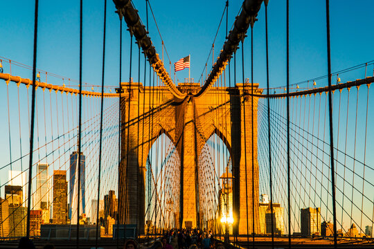 Iconic Brooklyn Bridge Towers Bathed in Golden Sunrise Light, Featuring American Flag and New York City Skyline