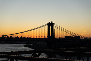 Fototapeta premium Iconic Manhattan Bridge Silhouetted Against a Radiant sunrise Sky, Casting a Dramatic Scene Over the East River in New York City.