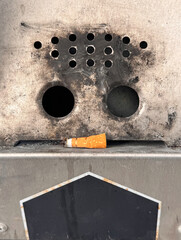outdoor ashtray, old rusty metal plate with two holes and cigarette butt looks like a face
