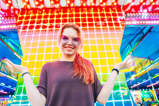Smiling girl in sunglasses at amusement park with neon grid lights