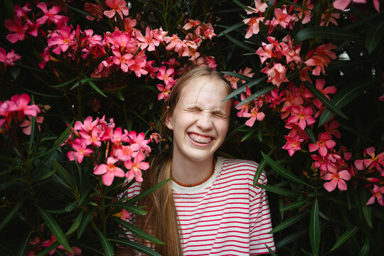 Smiling girl with braces in striped shirt surrounded by pink blossoms outdoors