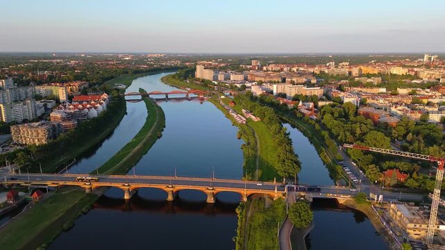 Aerial view over Wrocław, Poland during golden hour showing multiple river bridges, modern riverside buildings, and tree-lined paths along the Odra River