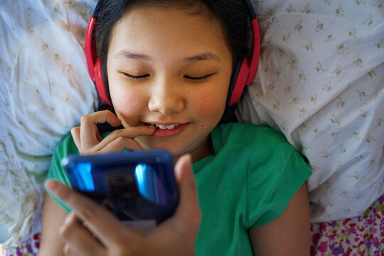 Girl with headphones relaxing on bed listening to music on smartphone